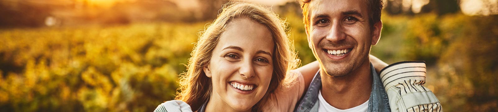 Young couple outdoors with field behind them.